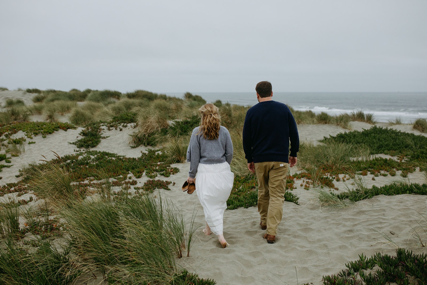 A couple walk away on a sand dune in San Francisco.