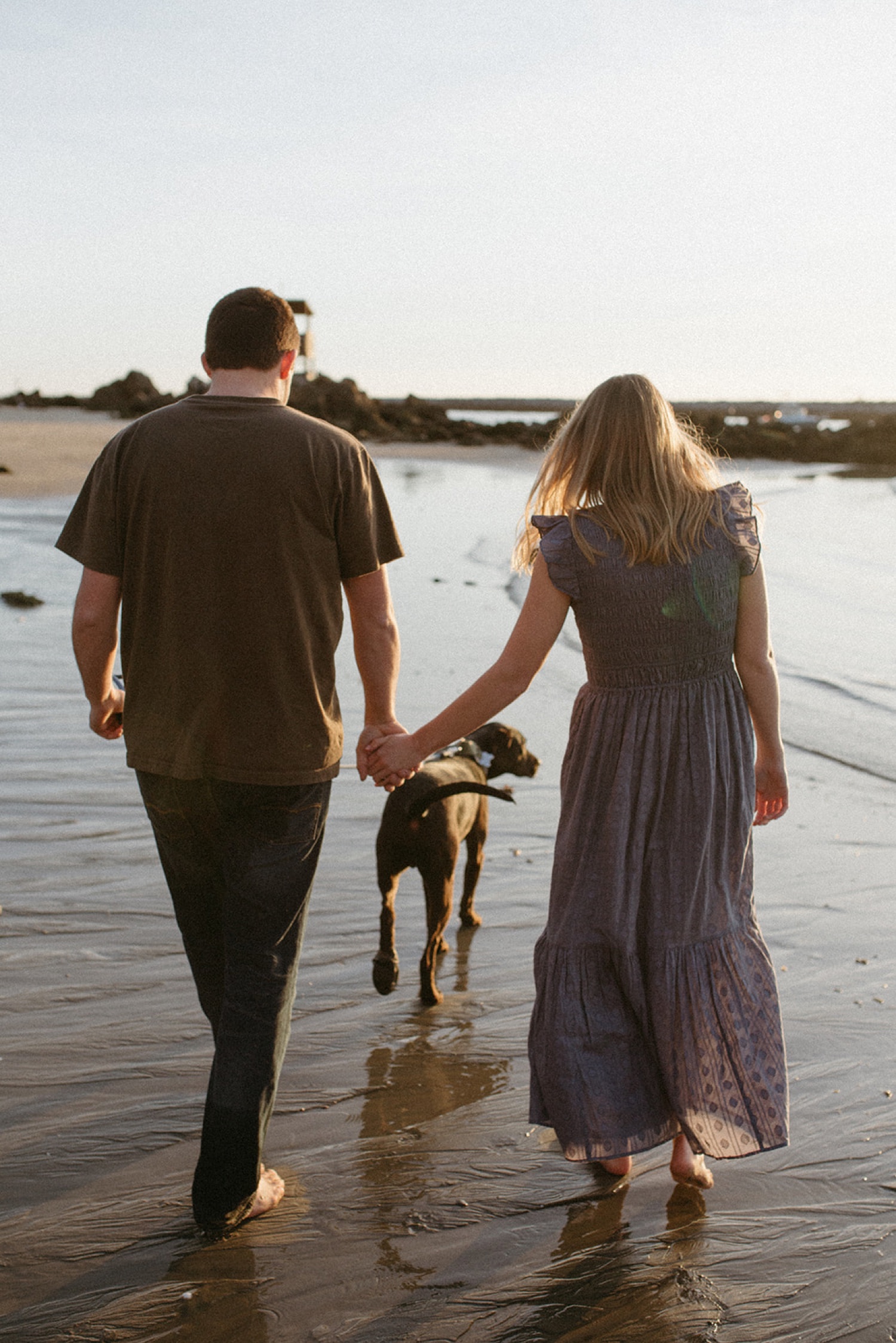 Couple walk on beach with their dog during their engagement photos